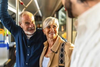 Happy senior couple standing on a city bus, smiling and chatting with another passenger while