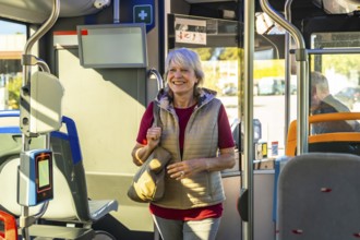 Senior woman standing, holding a bag, and smiling while traveling on a modern public transit bus,