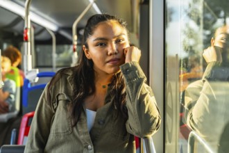 Young woman riding public transport contemplating and looking at camera while warm sunlight