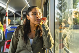 Young woman passenger traveling on a public transport bus, looking out of the window with a pensive