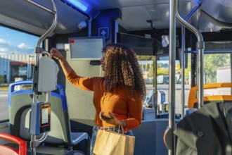 Young woman with curly hair validating her public transport ticket on a bus, holding a smartphone