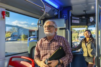 Senior male passenger holding a digital tablet and phone, smiling and looking out the window while