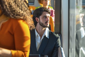 Man with beard and dark hair traveling by bus, looking thoughtfully out the window with his