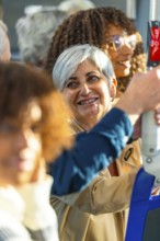 Mature woman with gray hair smiling on a city bus, holding a handrail amid diverse passengers,