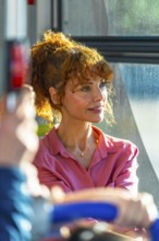 Redhead woman on a city bus, bathed in warm sunlight as she gazes out the window, relaxed and