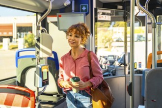 Woman standing on a city bus during the morning commute, holding a reusable coffee cup and brown