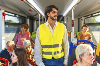 Man wearing a high visibility vest standing on a public transport bus, looking out the window while