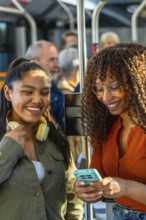 Two young adult women smiling and looking at a smartphone, enjoying public transportation while