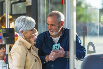 Senior couple standing on a city bus, smiling and sharing a smartphone as they browse together,