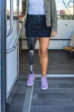Woman with a prosthetic leg standing inside a public transport bus, holding onto a handrail,