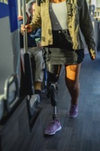 Woman with prosthetic leg and athletic shoe standing on a city bus, holding the handrail while
