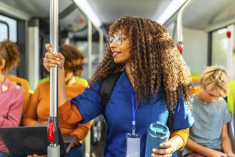 Healthcare professional with curly hair standing in a public transport bus, wearing scrubs while