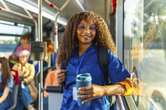 Smiling female nurse or doctor in scrubs and a backpack holding a travel mug, riding public