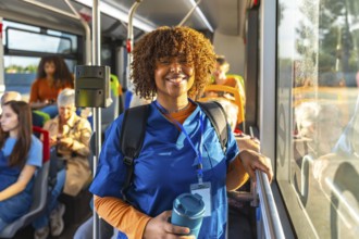 Young black woman doctor or student nurse standing on a public transport bus, wearing blue scrubs,