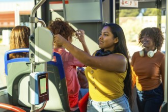 Young women traveling on a bus, smiling and interacting with a contactless payment ticketing