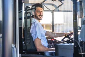 Young man working as a bus driver, smiling at the viewer while steering the public transport