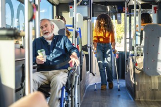 Senior man in a wheelchair and young woman using crutches traveling together on an accessible city