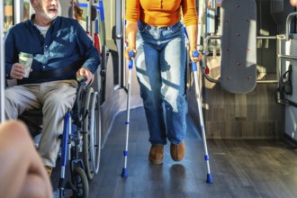 Senior man in wheelchair and woman with crutches navigate a busy city bus aisle together,