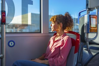Woman seated on a city bus, gazing out the window in quiet thought during commute as sunlight