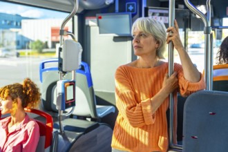 Senior woman standing on a public transport bus, holding a pole and looking out the window,