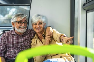 Happy senior couple on a bus, smiling and pointing out the window while enjoying a relaxed city