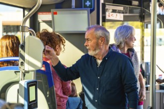 Senior man tapping a contactless fare card on a validator aboard a city bus, surrounded by fellow