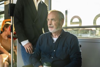 Senior man on a city bus, seated by the window with a reusable cup, gazing thoughtfully outside