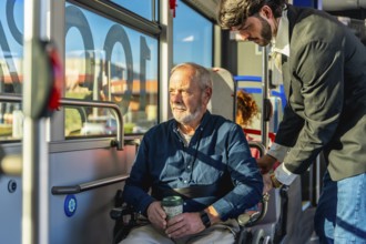 Employee assisting a senior man in a wheelchair on public transport, securing his position for a