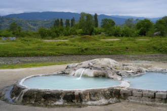 Hot spring pool surrounded by green landscape and forested mountains in the background, springs of