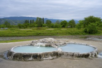 Hot spring pool in open landscape with wooded hills and mountains in the background, springs of