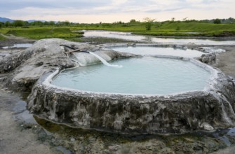 Hot spring pool in natural landscape with vast meadows and cloudy sky, springs of Amaghleba,