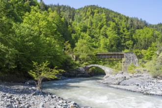 River flows under a car and stone bridge amidst green forests, Purtio stone arch bridge,