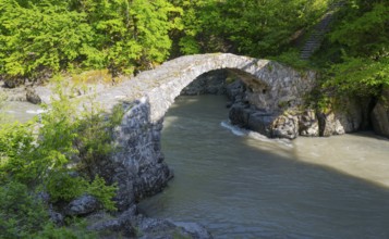Old stone bridge spanning river in a green forest area in sunshine, Purtio stone arch bridge,