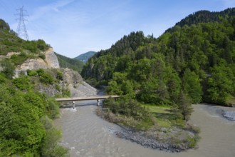 A wide river flows under a bridge through wooded hills while a power line crosses the rocky