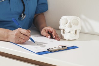 A medical professional reviews the patient's documentation, making notes. There is a model of a