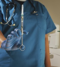 The dentist, in a blue lab coat and gloves, holds a carpal syringe in front of him