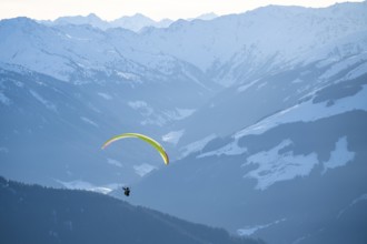 Paragliders flying over snowy mountain peaks in winter in evening light, Kitzbühel Alps, Tyrol,
