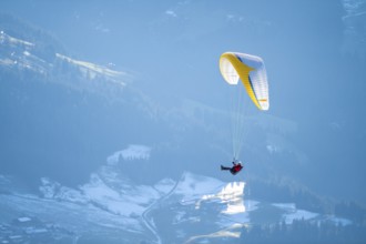 Paraglider flying over snowy mountains in winter in evening light, Kitzbühel Alps, Tyrol, Austria