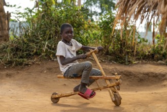 Child on a wooden scooter, homemade toy, in a traditional village, Sadaani, Tanzania