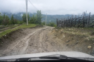 Muddy dirt road in a rural area leads through nature, four-wheel drive Lada, Imereti region,