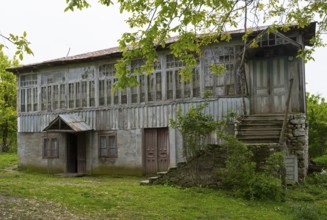 Old wooden house with lots of windows surrounded by trees in the countryside, Imereti region,