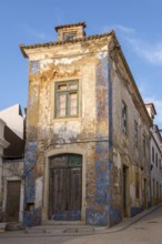 Abandoned building with peeling façade and blue paint residues under clear sky, Ericeira, Portugal