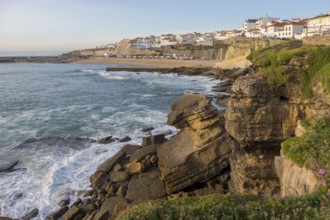 Coastal town with rocky cliffs by the sea and calm water at sunset, coast near Ericeira, Portugal