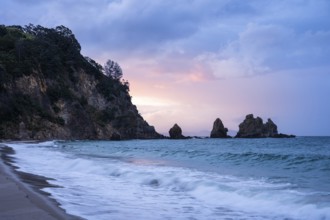 Landscape with sea, rocks and sandy beach in New Zealand in the evening at sunset. Otama Beach,