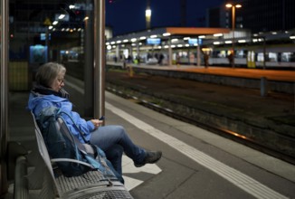 Night shot, elderly woman, traveler, sitting alone on a bench on a platform, backpack, using
