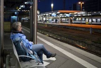 Night shot, elderly woman, traveler, sitting alone on a bench at the platform, backpack, main train