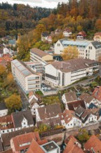 Modern buildings next to older residential buildings in autumn surroundings near wooded hills,
