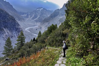 Female hiker on mountain trail in autumn-colored surroundings with the Mer de Glace glacier,