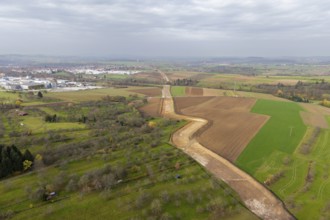 Aerial view of a rural area with fields and a city in the background under cloudy sky, construction