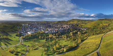 Aerial view of a village on hilly terrain with green fields and cloudy sky, autumn,